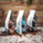 Three bags of signature Foxtail Coffee beans on a pile of loose coffee beans against a wooden backdrop.